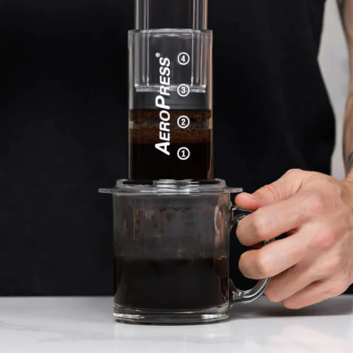 AeroPress Clear coffee maker pressing coffee into a glass mug, held steady by one hand