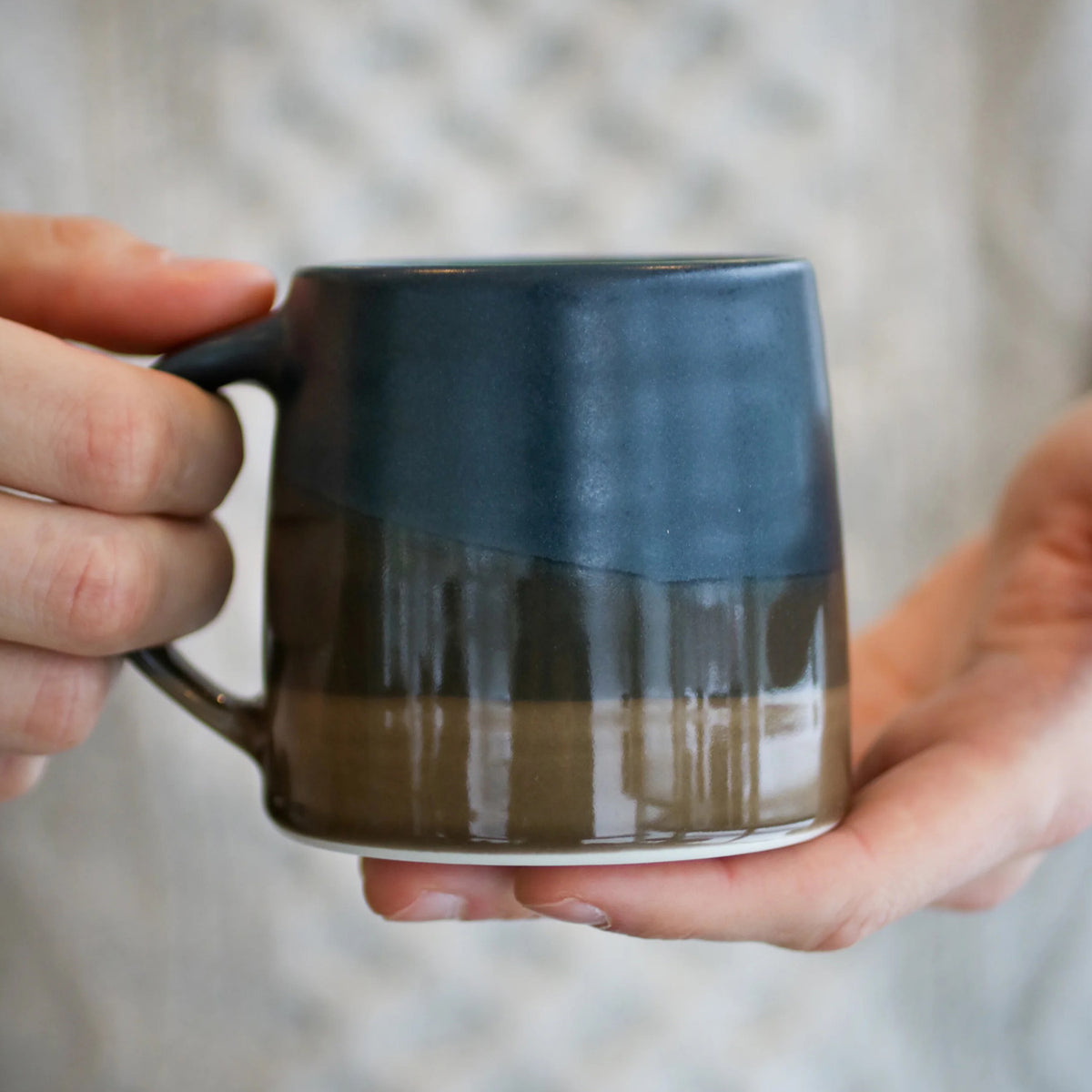 Kinto ceramic mug with a two-tone blue and brown glaze, held in two hands